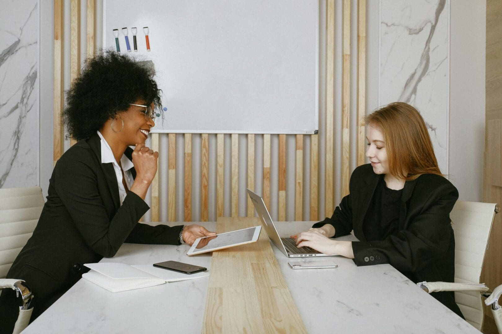 Two women sitting at a table with laptops.