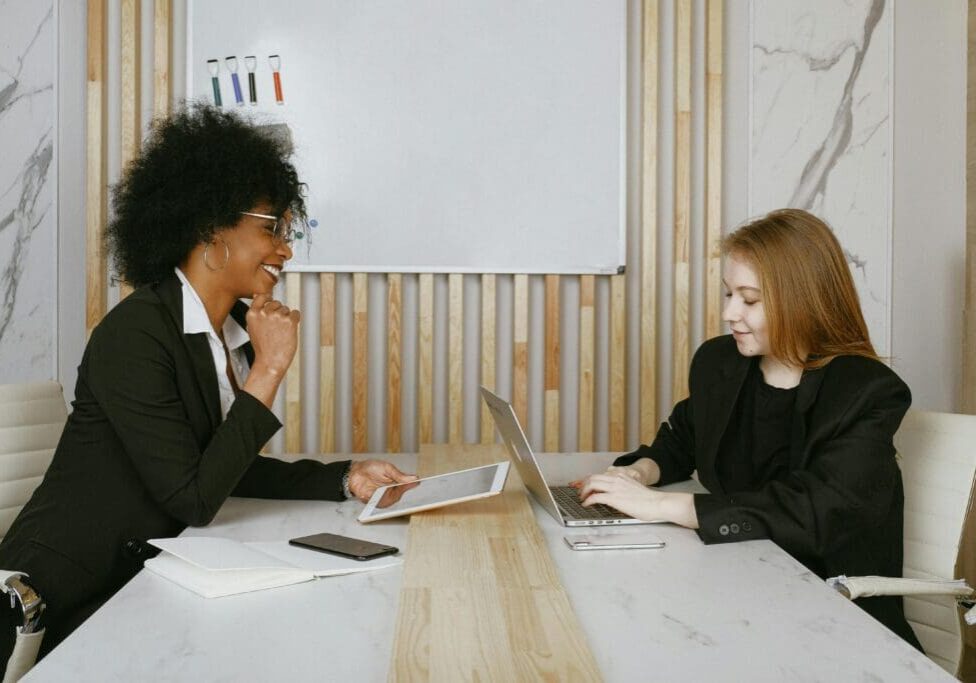 Two women sitting at a table with laptops.